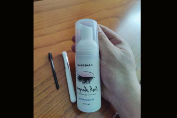 hand which hold  gentle eyelash extension cleanser  with brush 